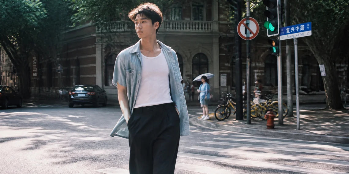 Young Asian man walking confidently on a sunny street wearing a stylish summer layered outfit.