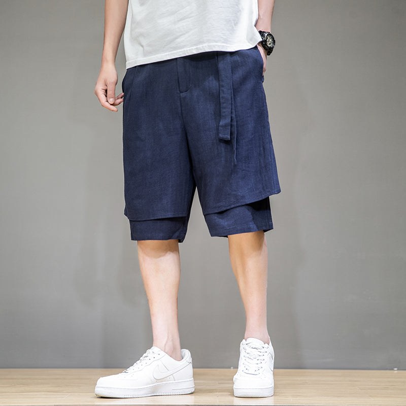 男模特微側面展示深藍色雙層棉麻五分褲，呈現自然垂墜的空氣感廓形與修飾身形的寬鬆版型。